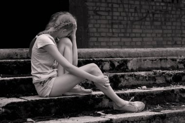 Monochrome photo. Offended upset girl teenager sits on old concrete ladder outsid