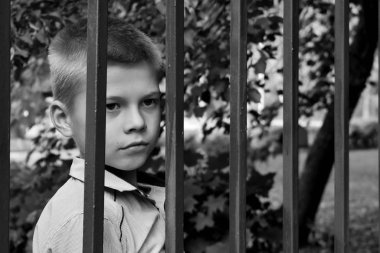 Monochrome photo. Sad boy behind fence. The boy's face behind bars. Deprivat