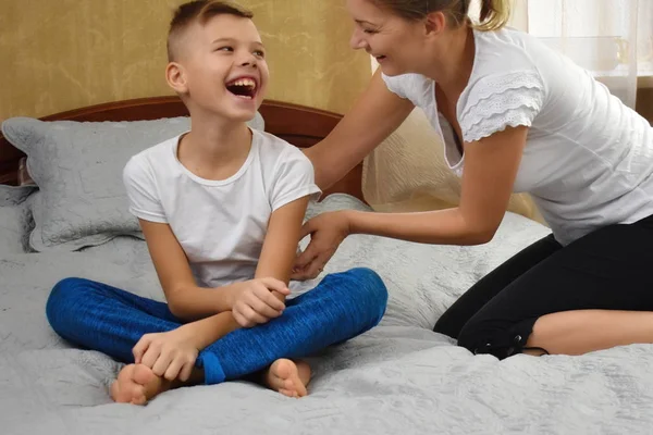 Mother tickling son. The parent teases the child. Fun games with mom. Mother and son on bed — Stockfoto