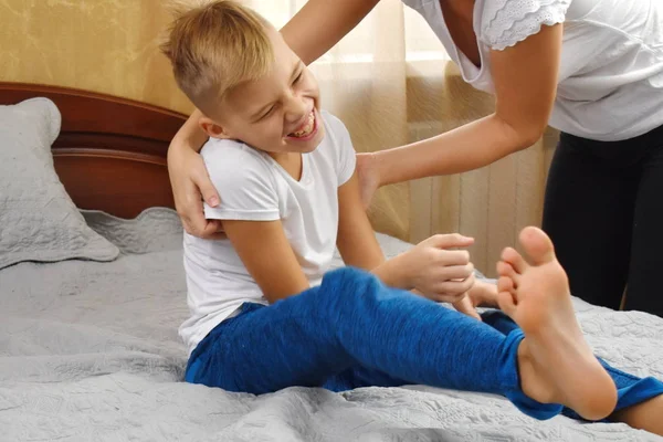 Mother tickling son. The parent teases the child. Fun games with mom. Mother and son on bed