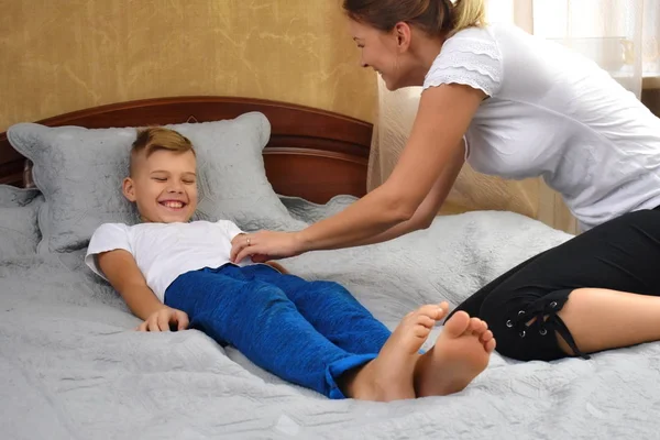 Madre cosquillas hijo. El padre se burla del niño. Juegos divertidos con mamá. Madre e hijo en la cama —  Fotos de Stock