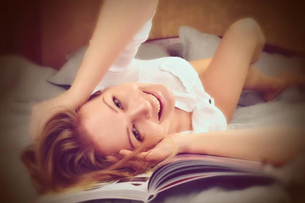 Happy woman lying on the bed. Pastime with a book at home. The woman smiles and enjoys happiness — Stockfoto