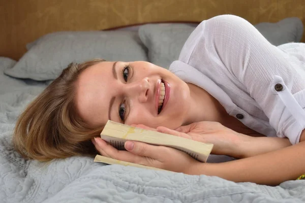 Mulher feliz na cama. A rapariga e o livro. Relaxar em casa um pouco — Fotografia de Stock