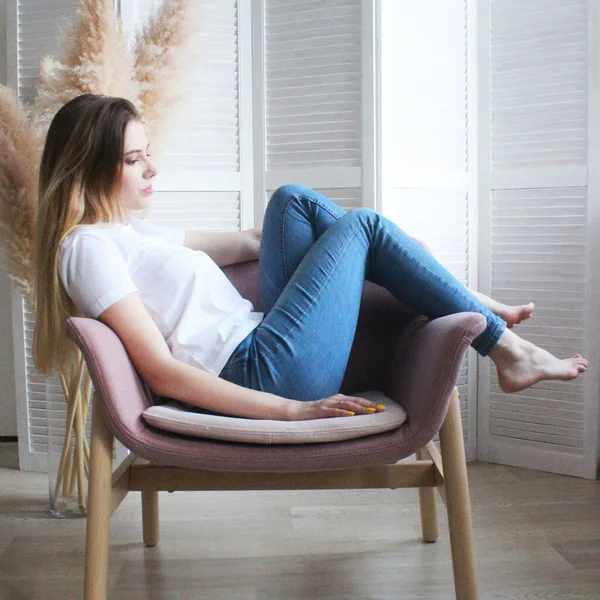 A senhora na cadeira ao lado do ecrã. A menina de jeans sentada em uma cadeira macia — Fotografia de Stock