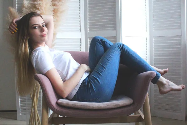 A senhora na cadeira ao lado do ecrã. A menina de jeans sentada em uma cadeira macia — Fotografia de Stock