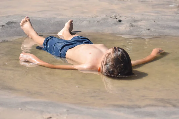 Chłopiec leżał w brudnej wodzie na ziemi. Dziecko bawi się w kałuży — Zdjęcie stockowe