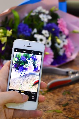 Çiçekçi buketin fotoğrafını çekiyor. Akıllı telefonunuzla çiçeklerin fotoğrafını çekiyorsunuz.