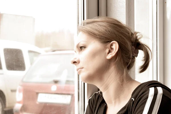 Mujer triste mirando por la ventana. Aislamiento. Un estado de emergencia en el país. La persona infectada — Foto de Stock