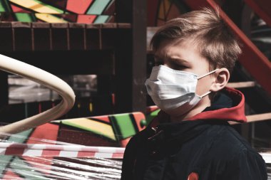 Çocuk parkında sağlık maskeli bir çocuk. Oyun parkı banda sarılı