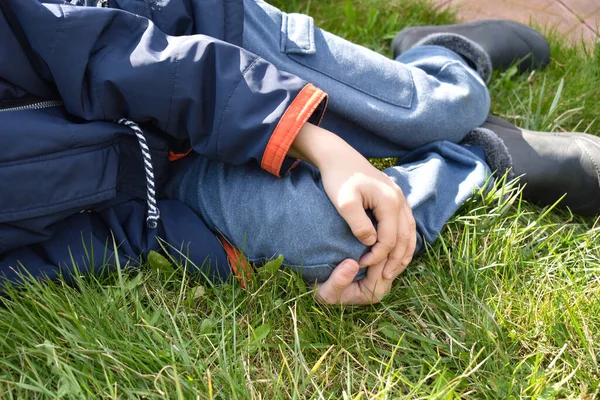 Le garçon est allongé sur l'herbe et s'accroche au genou. Le bébé s'est blessé à la jambe — Photo