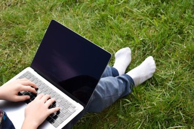 Uzaktan eğitim otomatik kapı. Çocuk çim üzerinde okul ödevleriyle meşgul. Sokakta dizüstü bilgisayarı olan çocuk.