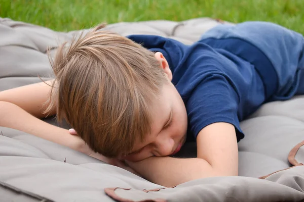 Спи на траве. Мальчик лежит на матрасе в саду. Отдых на открытом воздухе — стоковое фото