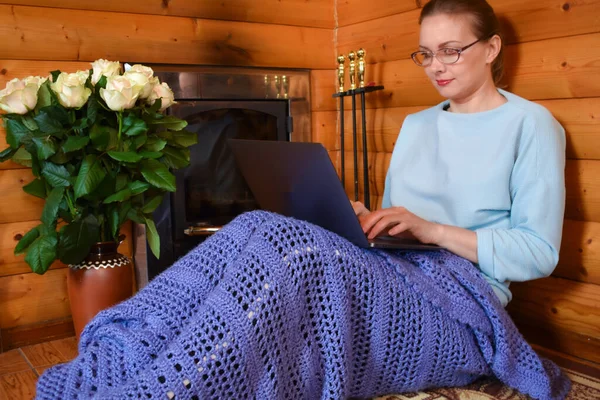 Mujer junto a la chimenea con un ordenador portátil. Un lugar acogedor para trabajar en casa. lugar de trabajo remoto —  Fotos de Stock