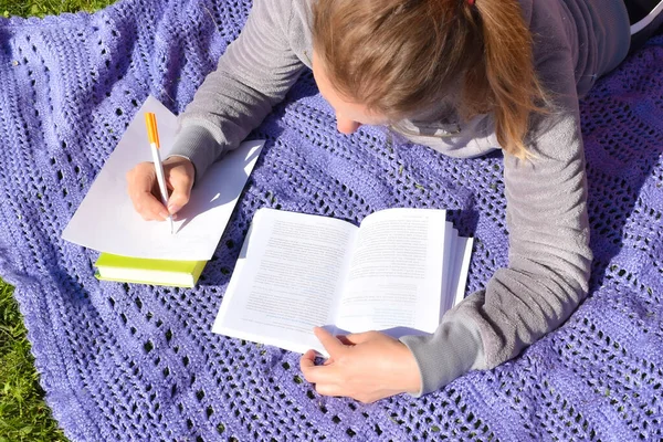 A woman writes out important notes from a textbook. student is preparing for a difficult exam in the summer.