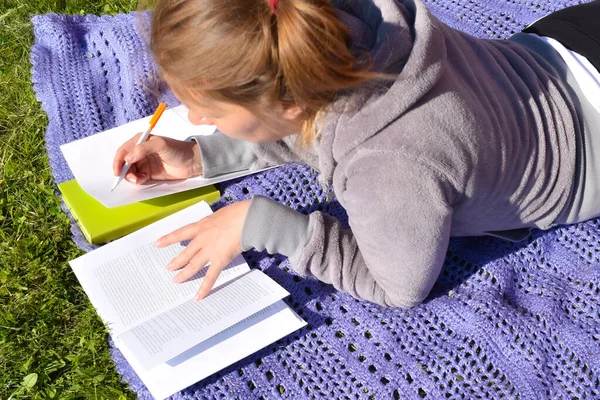 En kvinna skriver viktiga anteckningar ur en lärobok. student förbereder sig för en svår tentamen på sommaren. — Stockfoto