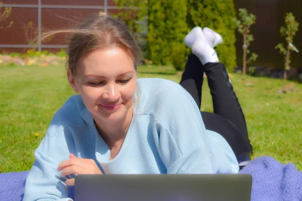 La comunicazione web. Donna sull'erba con computer portatile che guarda lo schermo. Soggiorno in giardino freelance — Foto Stock