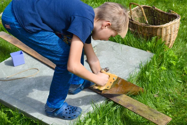 Pojke sågar trä. En pojke jobbar i trädgården. Barnverkstad utanför — Stockfoto