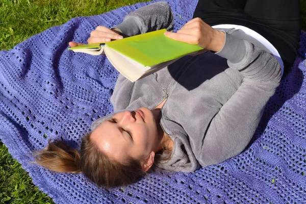 Het meisje ligt op een deken met een boek in de tuin op gras. Liefde voor literatuur — Stockfoto