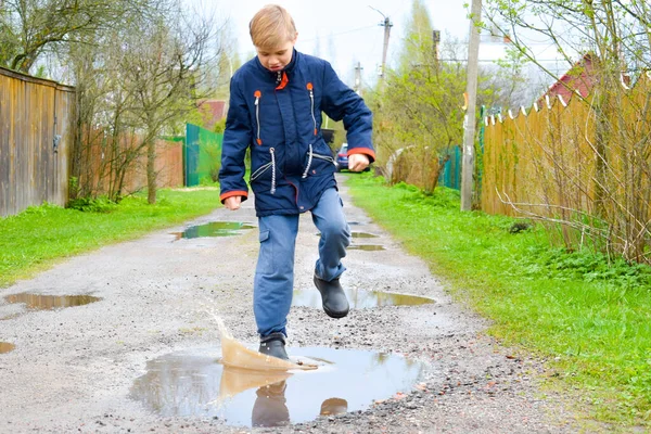 Pojkbarnet stöter på en våt pöl. Rolig promenad. — Stockfoto