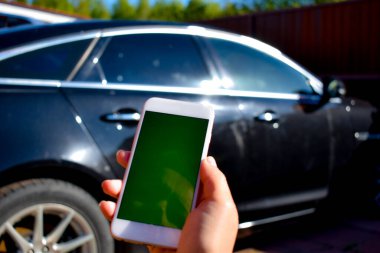 Kız arka planda elinde bir akıllı telefon tutuyor. Siyah bir araba.