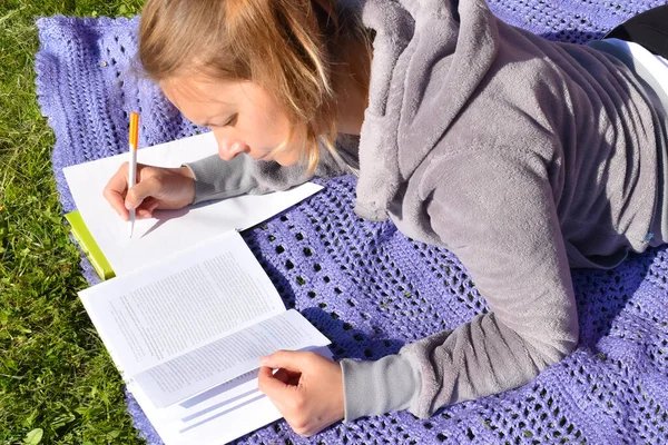 En kvinna skriver viktiga anteckningar ur en bok. Studera och studera i parken — Stockfoto