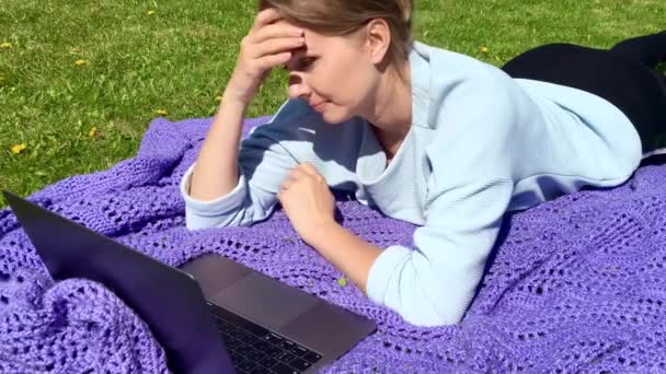 A woman working at a laptop on the grass outside remotely — Stock Video