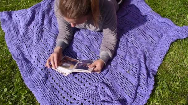 夏に公園の毛布の上に紙の写真アルバムを持つ女性。家族の思い出 — ストック動画