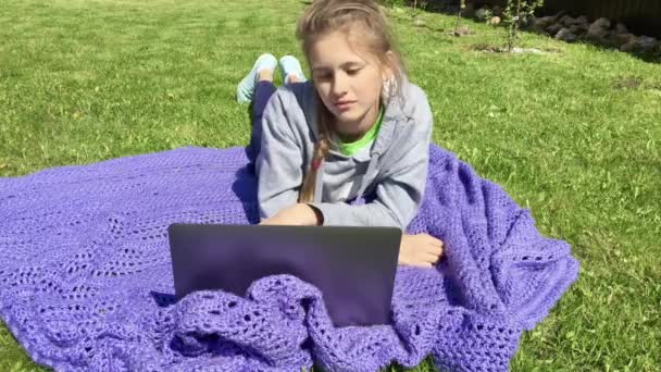 Fille regarder des leçons en ligne sur l'ordinateur portable sur une couverture dans le jardin . — Video