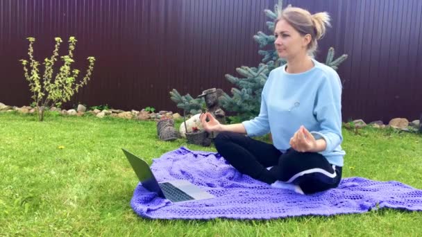 Woman in Lotus position on the grass in front of laptop. Video health lessons — Stock Video