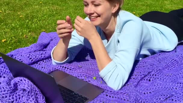 Mujer joven acostada en una manta con portátil y hablando con alguien en la pantalla — Vídeo de stock