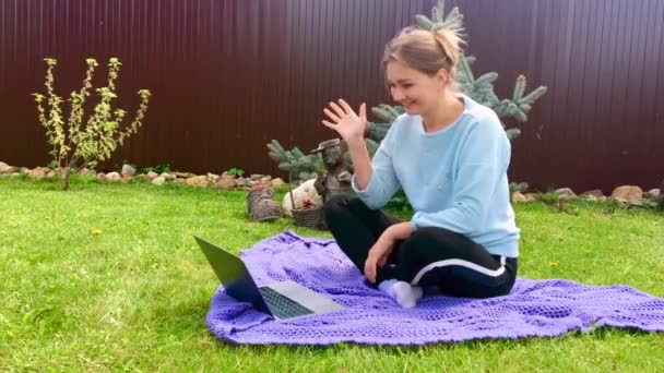 Een vrouw op het gras die aan een laptop werkt. Werk op afstand op de computer buiten. — Stockvideo