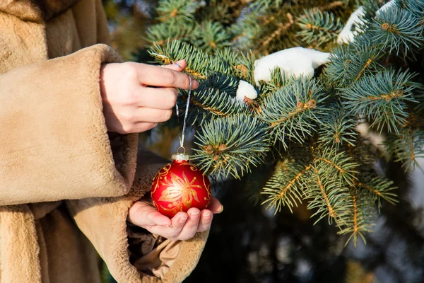 Vrouw opknoping van een rode kerst bal op fir closeup. — Stockfoto