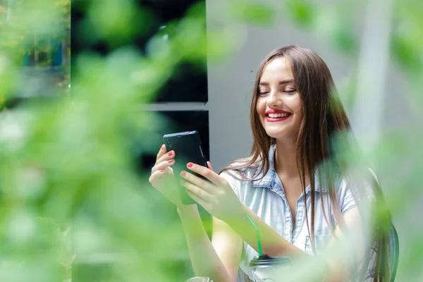 Sonriente chica joven utilizando el teléfono inteligente en la cafetería al aire libre — Foto de Stock