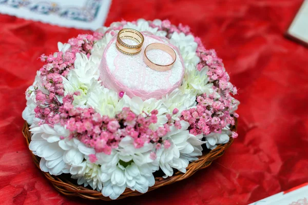 Anéis de casamento em um posto de flores em uma mesa vermelha — Fotografia de Stock