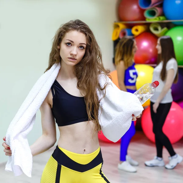 Mujer joven con una toalla sosteniendo una botella de agua en un gimnasio . —  Fotos de Stock