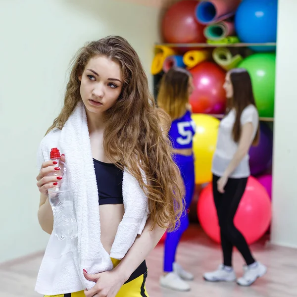 Mujer joven con una toalla sosteniendo una botella de agua en un gimnasio . —  Fotos de Stock