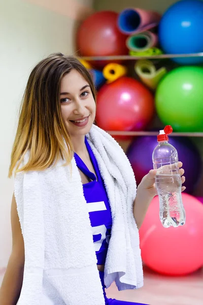 ジムで水のボトルを保持しているタオルを持つ若い女性 — ストック写真
