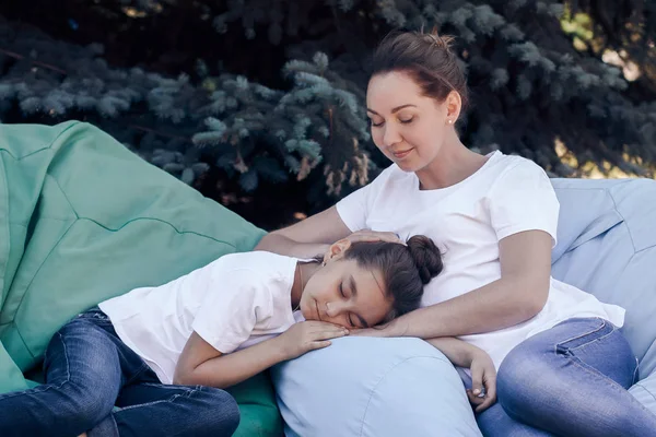 Tired mother and daughter relax on cushions in the park.