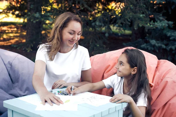 Smiling mother and daughter drawing sitting in park at summer da