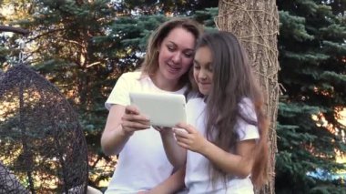 Mutlu anne ve kızı beyaz kullanarak tablet Pc, bir parkta otururken yaz gününde