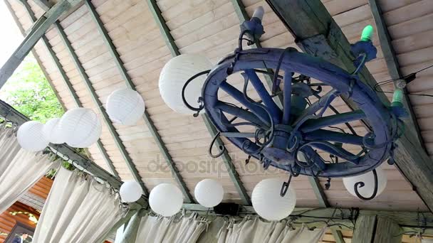 Hvide bolde og et træhjul med stearinlys hænger på loftet. Rustik udsmykning af restauranten . – Stock-video