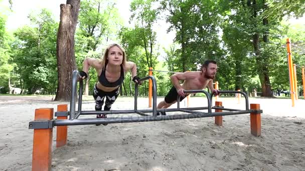 Young sportive woman and bearded man doing push-ups exercises in a parrk at summer day. — Stock Video