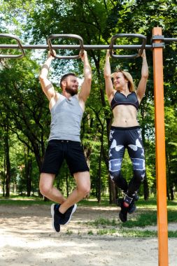 Genç sportif kadın ve sakallı adam pull-up egzersizleri yapıyor