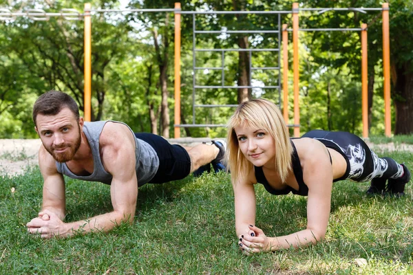 Joven pareja atractiva haciendo ejercicio tablón en el parque juntos . —  Fotos de Stock