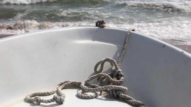 Old row boat on seaside. Windy weather, waves in the sea bay. Rope close up. — Stock Video