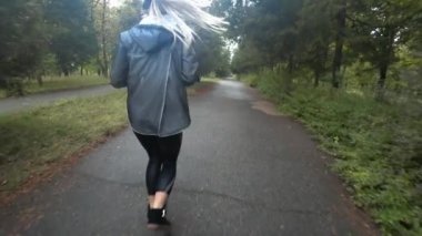 Uzun saçlı sarışın kız yağmurlu gün, parkta çalışıyor güzel genç dinle müzik kulaklık, spor, sağlıklı bir yaşam tarzı yapıyor... Ağır çekim.