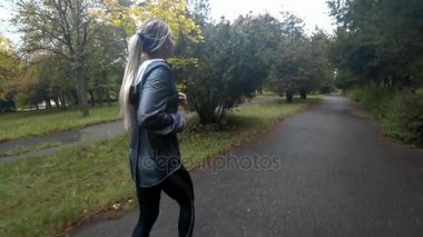 Güzel genç sarışın kız parkta spor, sağlıklı bir yaşam tarzı yapıyor yağmurlu bir gün, çalışıyor... Ağır çekim.