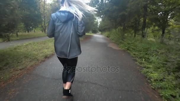 Belle jeune fille blonde aux cheveux longs court dans le parc le jour de la pluie, écouter de la musique au casque, faire du sport, un mode de vie sain.. Mouvement lent .