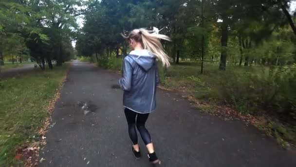 Mooie jonge blonde meisje draait in park op regenachtige dag, sport, een gezonde levensstijl te doen... Slow motion. — Stockvideo