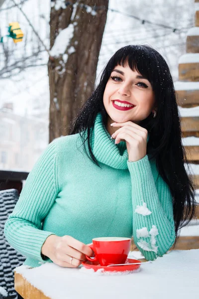 Attractive young woman drinks a coffe in street cafe at snowy wi